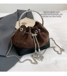 Détail du sac seau en daim avec poignée en métal argenté et chaîne sur un blazer