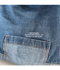 Détail du tissu denim bleu montrant les coutures orange et la texture de la poche