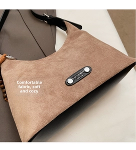 Détail du sac à bandoulière en daim marron souple avec bordure noire et plaque logo