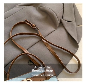 Detail of adjustable brown leather shoulder strap with silver buckle on denim bucket bag