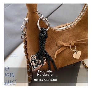 Detail of suede crescent bag featuring silver hardware and heart charms with woven cord