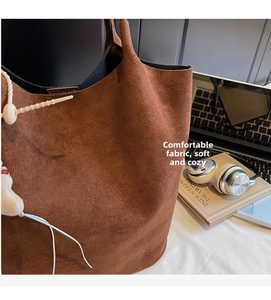 Close-up of brown suede tote bag with textured finish and white decorative pendant