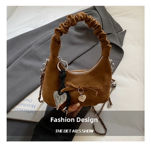 Detail of suede crescent bag showing heart charms and pleated handle on a grey blazer