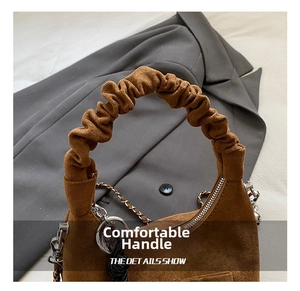 Close-up of brown suede crescent bag featuring a ruched handle and metal chain strap