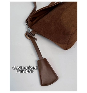 Detail der dunkelbraunen Wildleder-Schultertasche mit Nähten und Lederanhänger mit Silberring
