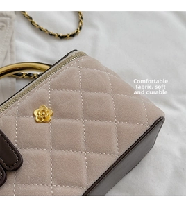 Detail of quilted suede crossbody bag featuring a golden camellia clasp and metal handle