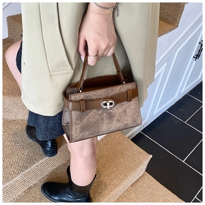 Detail of a brown leather handbag with frosted texture and silver turn-lock closure