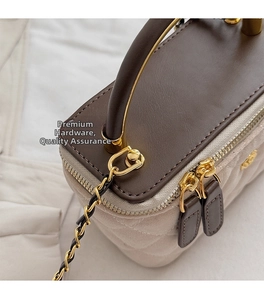 Close-up of golden dual zippers and hardware on a quilted beige and brown box bag
