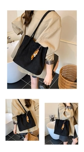 Detail of minimalist black tote bag featuring wooden bead tassel and slender shoulder straps