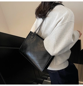 Detail view of the black quilted tote bag featuring glossy leather and chain strap