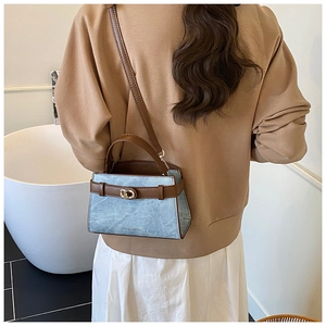 Detail view of stylish light blue marbled handbag with brown leather strap and gold buckle