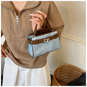 Detailed view of blue denim handbag with brown leather accents and gold twist lock clasp