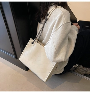 Dettaglio delle cuciture a V color crema e della tracolla a catena della borsa tote