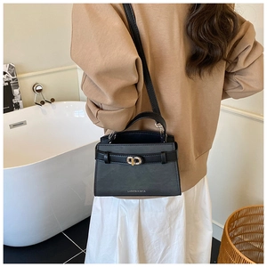 Detail of a black leather crossbody bag with a gold metal clasp and adjustable strap