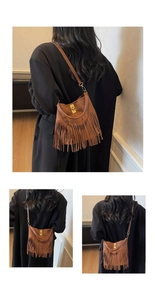 Detail of brown suede crossbody bag featuring retro tassels and gold buckle accents