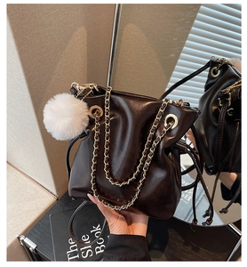 Détail du sac seau en cuir foncé avec chaîne dorée et charm pompon en fourrure blanche