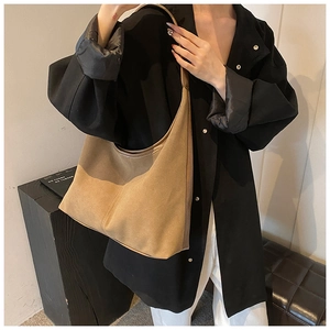Sac hobo en daim marron porté avec chemise noire et pantalon blanc chic