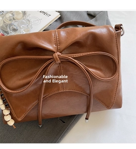 Detalle de bolso bandolera de cuero marrón con lazo grande y borla de cuentas de madera