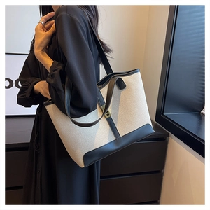 Close-up of canvas tote bag with black leather trim and elegant gold metal buckle