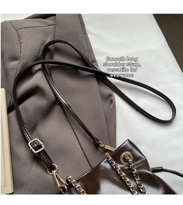Detail of smooth adjustable leather strap and gold chain on dark brown bucket bag
