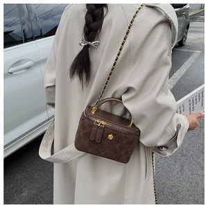 Detail of dark brown quilted suede crossbody bag with gold chain strap and floral accent