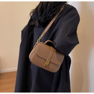 Close-up of brown litchi pattern leather handbag with gold metal lock and top handle