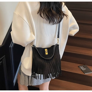 Detail of black suede tassel bag with gold twist lock worn by a model on stairs