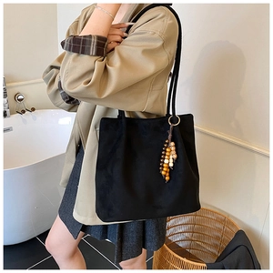 Detail of black suede tote bag with retro wooden bead charm and long shoulder strap