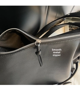 Close-up of black pebble leather tote featuring silver metal zipper and tassel detail