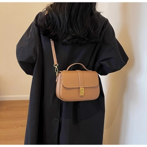 Detail of vintage brown pebble leather crossbody bag with gold metal lock on black coat