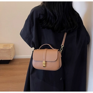 Detail view of brown pebbled leather crossbody bag with golden twist lock on black coat