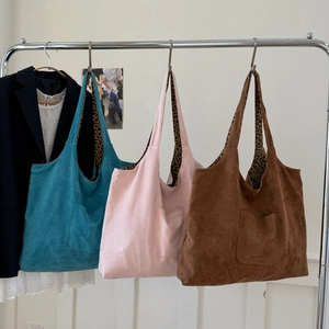 Three suede tote bags in teal, pink, and brown with leopard print lining hanging indoors