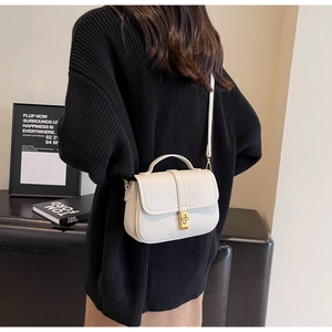 Close-up of off-white lychee grain leather crossbody bag with elegant gold twist lock