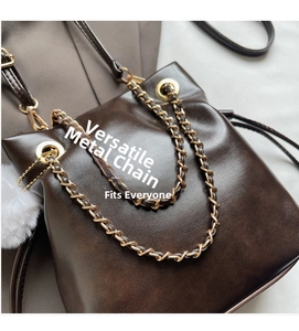 Detail of dark brown leather bucket bag with gold chain and white plush charm