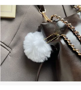 Close-up of shiny dark brown bucket bag with gold chain strap and soft white faux fur charm