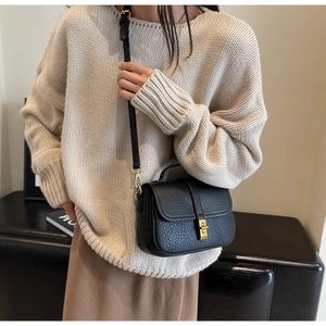 Close-up of black pebble leather crossbody bag with gold buckle on white knit sweater