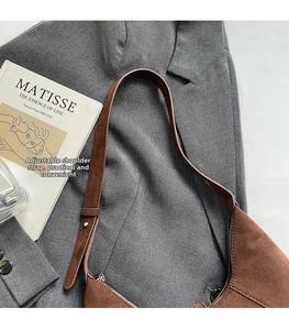 Close-up of brown faux suede shoulder bag with adjustable strap on grey blazer