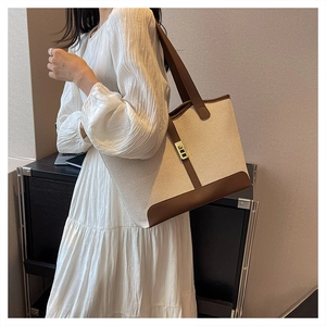 Detail of large beige canvas tote bag with brown leather handles and golden lock on model
