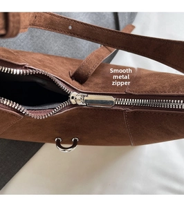 Macro shot of silver metal zipper and D-ring on brown suede leather underarm bag
