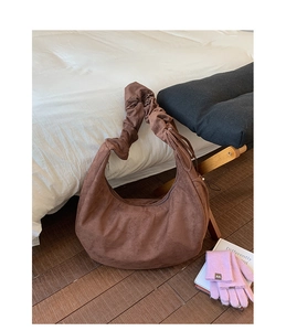 Detail of soft brown suede crescent bag with pleated cloud shoulder strap on wooden bench