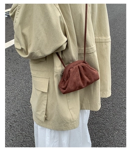 Braune Wildleder-Wölkchentasche kombiniert mit Khaki-Jacke und weißem Rock auf einer Straße