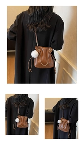 Detail of brown leather drawstring bucket bag with white pom-pom charm and chain strap