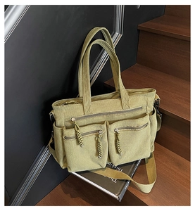 Detail view of multi-pocket green corduroy tote bag with woven zipper pullers on stairs