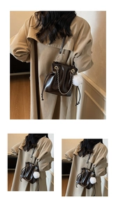 Detail of dark brown drawstring bucket bag with metal chain and plush ball charm
