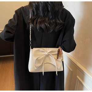 Detail of crossbody bag with oversized bow and beaded tassel charm on a model