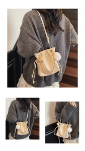 Detail view of cream drawstring bucket bag with gold chain and white fur pompom charm
