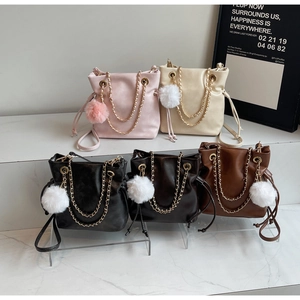 Detail of drawstring bucket bags with plush pom-poms and metal chain straps in five colors