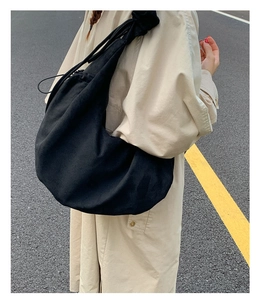 Street style view of a black drawstring tote bag worn as a large crossbody shoulder bag