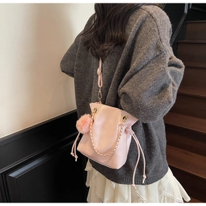 Detail of pink PU bucket bag with gold chain strap and fluffy pom-pom charm on side