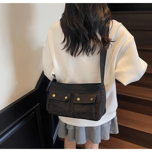 Close-up of black crossbody bag with large front pockets and gold metallic snap buttons
